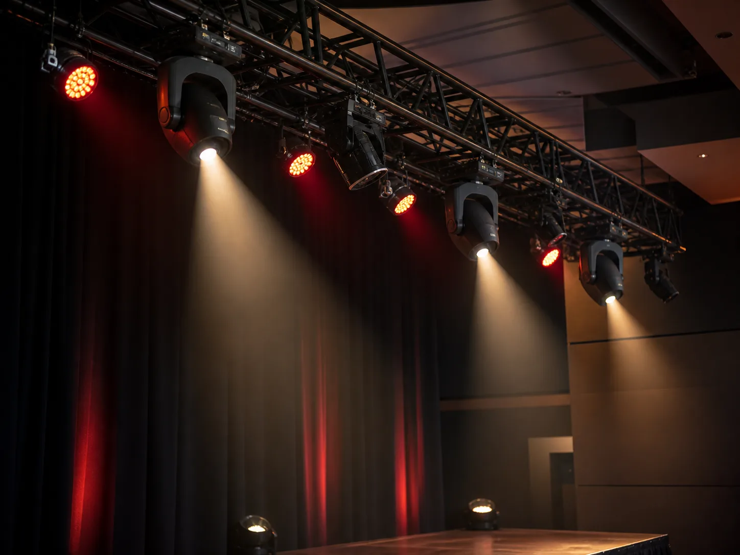 Stage lights on a truss casting red and warm beams
